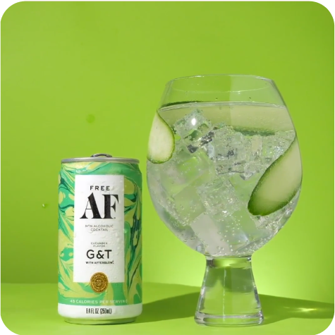 A canned beverage beside a glass with ice, lime, and cucumber slices on a green background.