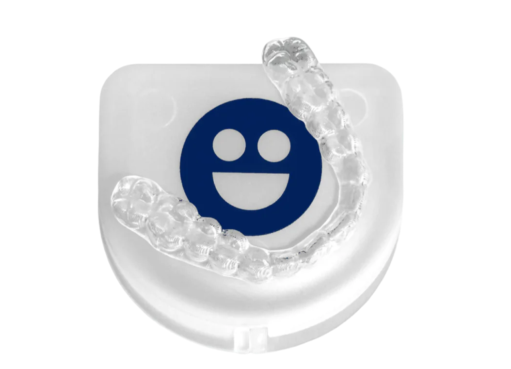 Clear dental aligner on a white case with a blue smiley face.