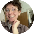 Person with glasses smiling in a room with a mirror.