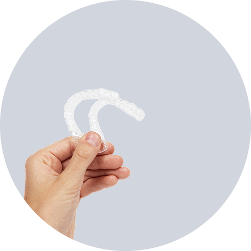 Hand holding two clear dental aligners against a light gray background.
