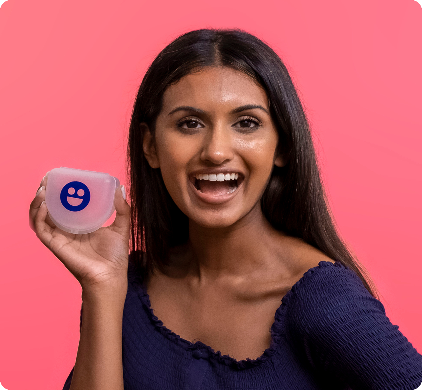 Person smiling, holding a small container with a smiley face, against a pink background.