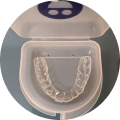 Clear dental aligner in a white case on a blue surface.