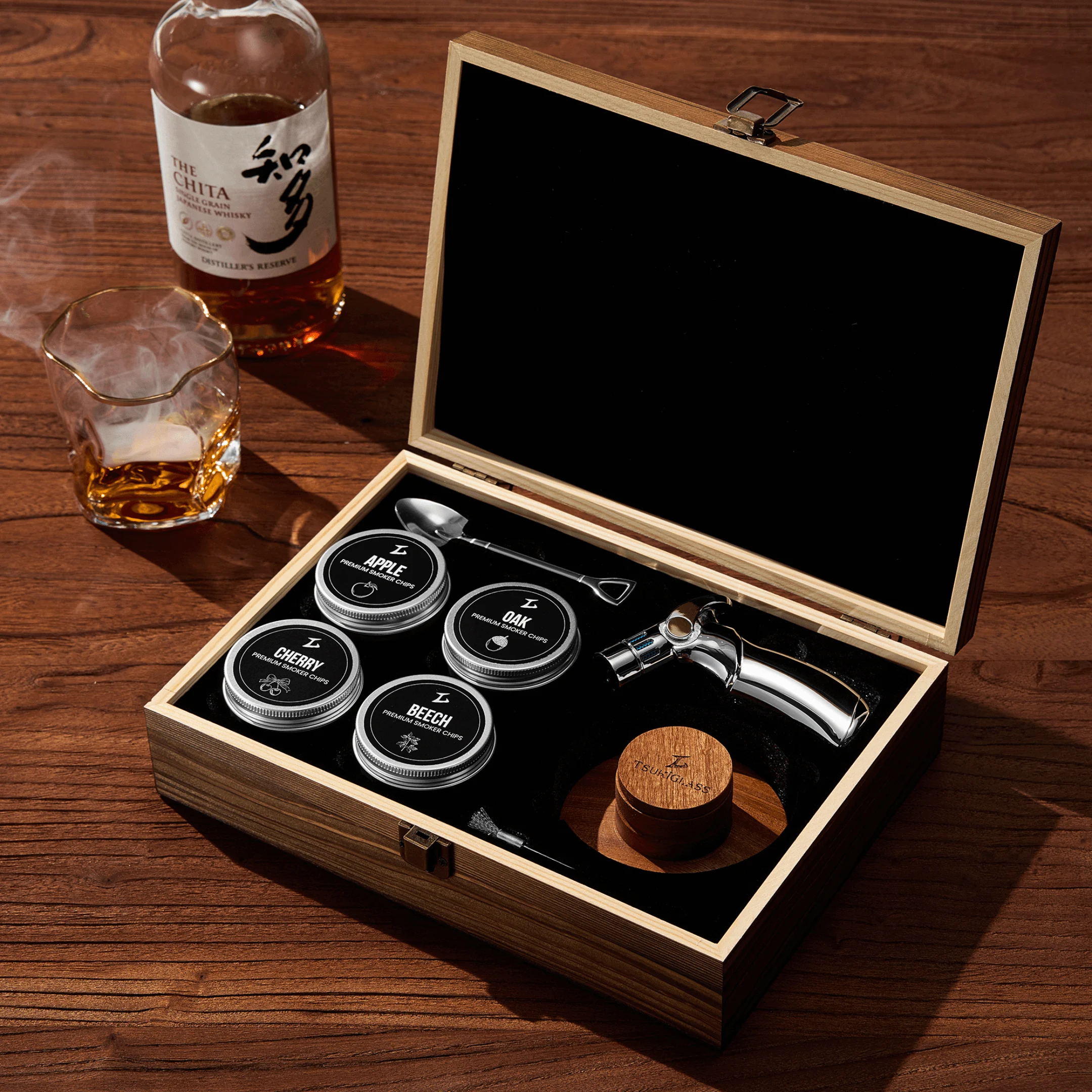 A cocktail smoker kit in a wooden box next to a bottle and a smoking glass of whisky.