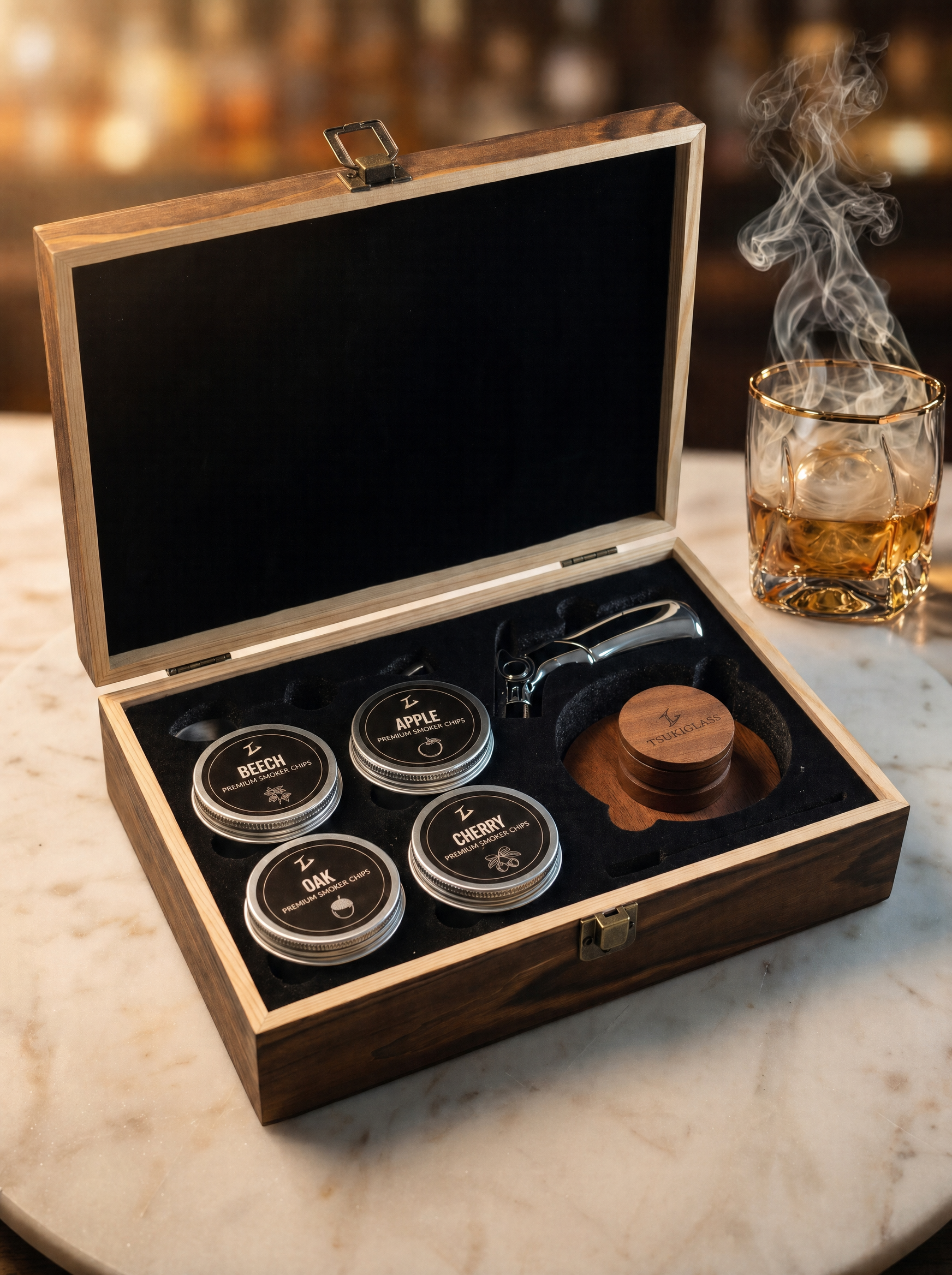 An open wooden box with a cocktail smoker set sits beside a smoking glass of whiskey.