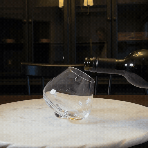 A bottle of wine, a decanter, and two glasses of spirits sit on a dark surface.