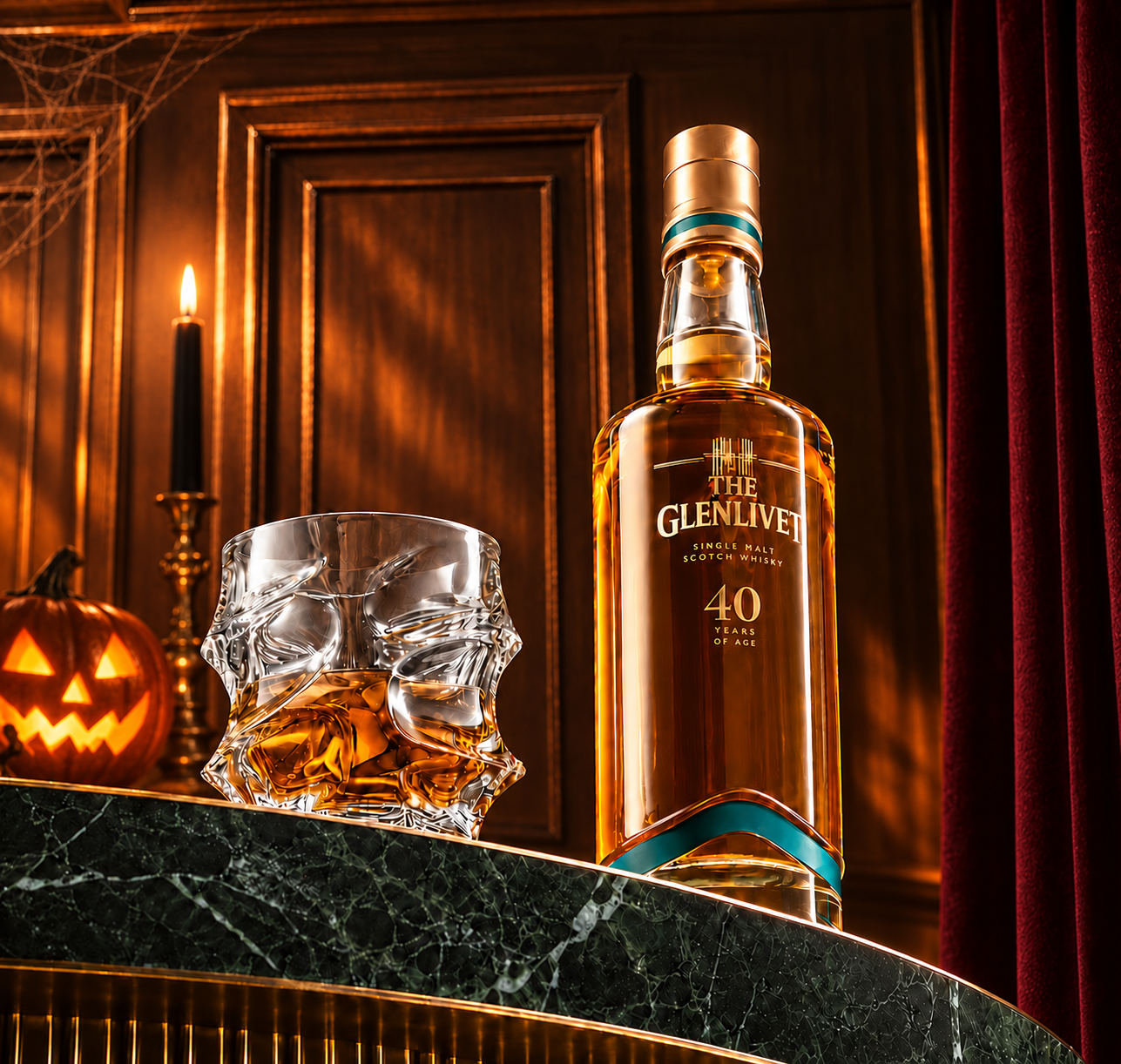 A bottle of The Glenlivet whisky sits next to a glass with Halloween decorations in the background.