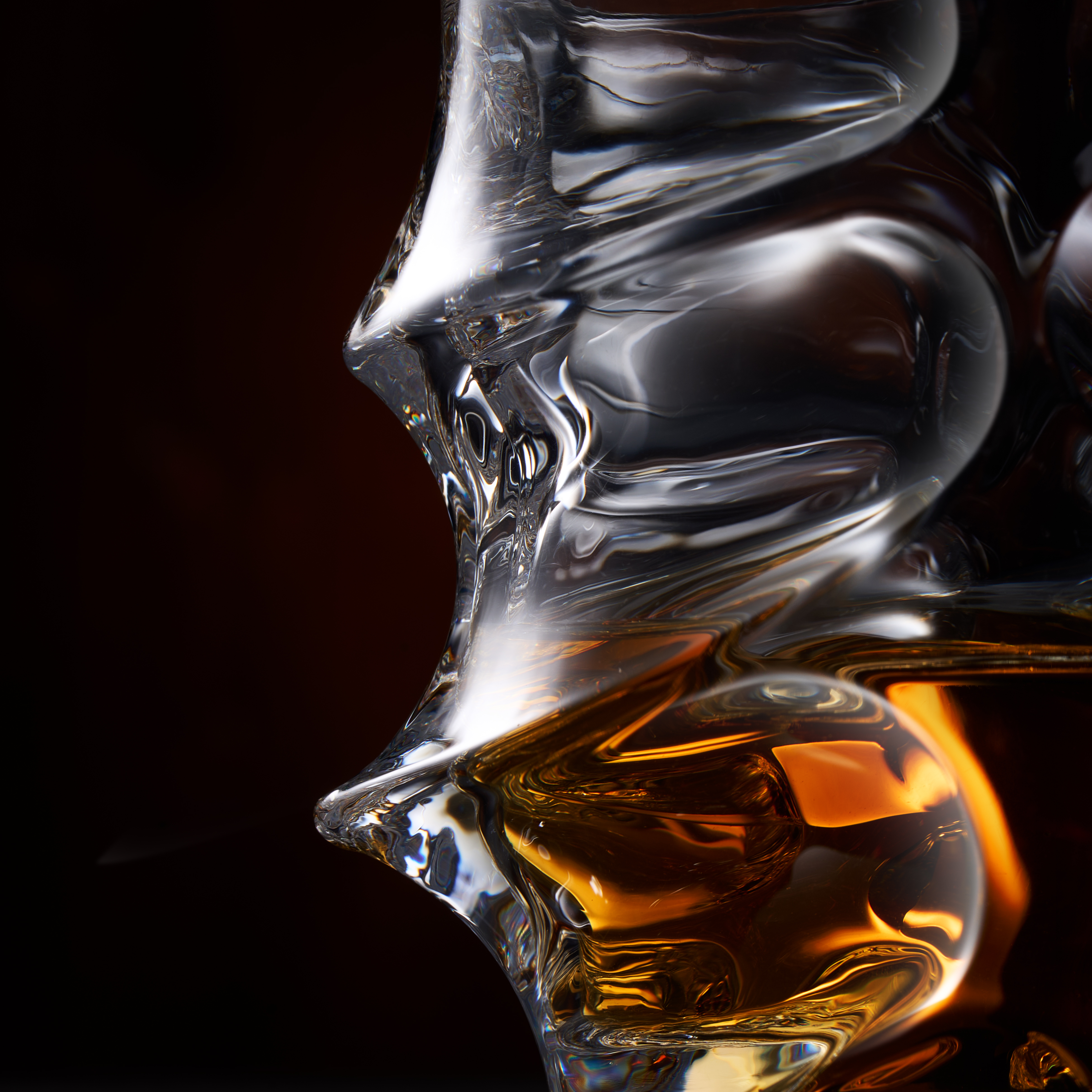 A close-up, abstract view of an amber liquid seen through a textured, sculpted glass against a dark background.