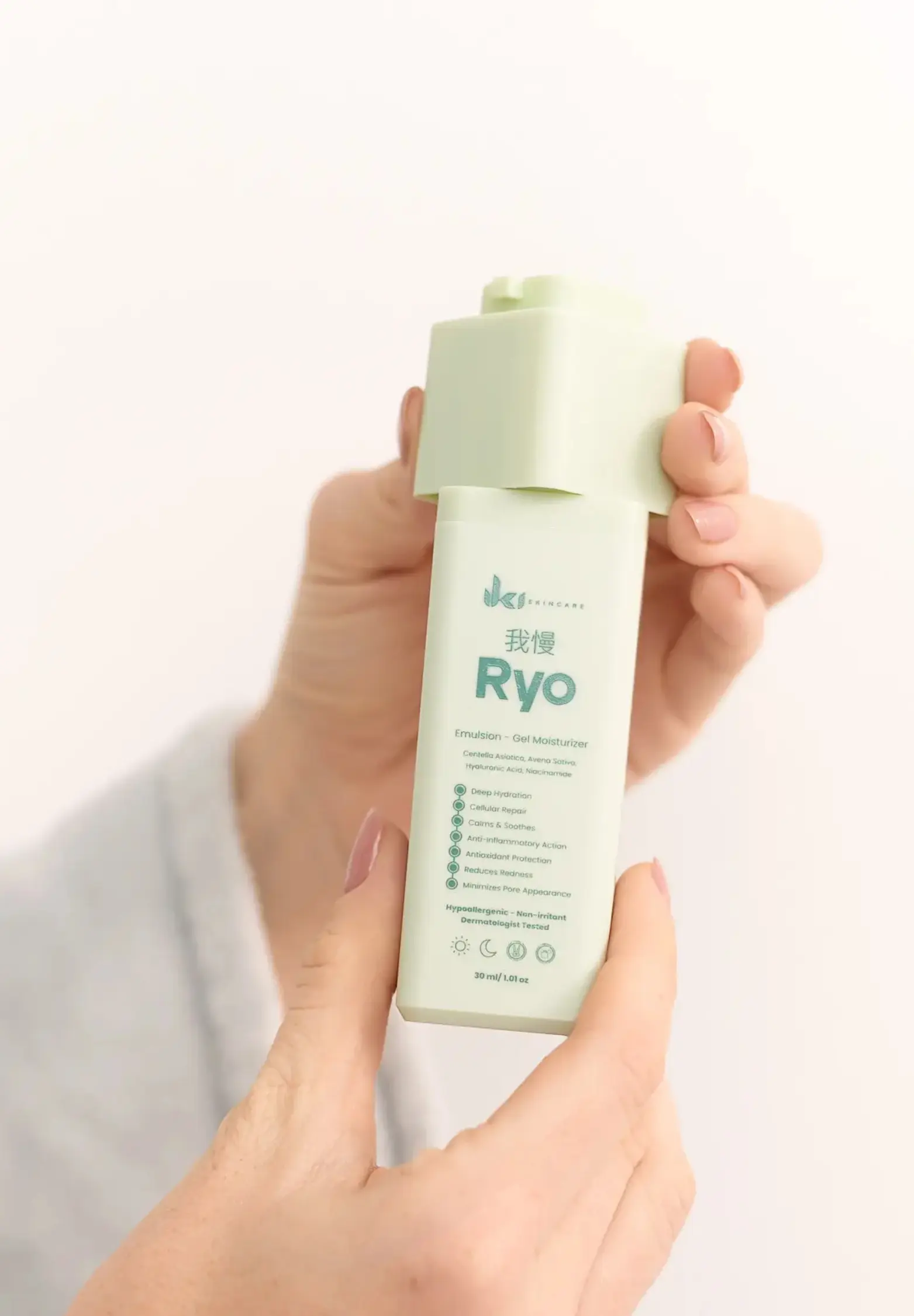 A person's hands hold a light green bottle of Ryo skincare product against a white background.