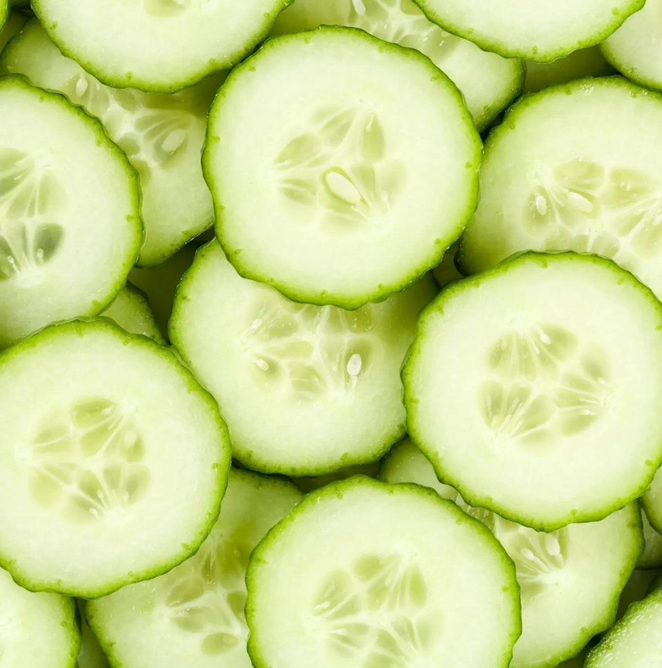 A close-up, top-down view of many overlapping, round slices of fresh green cucumber.