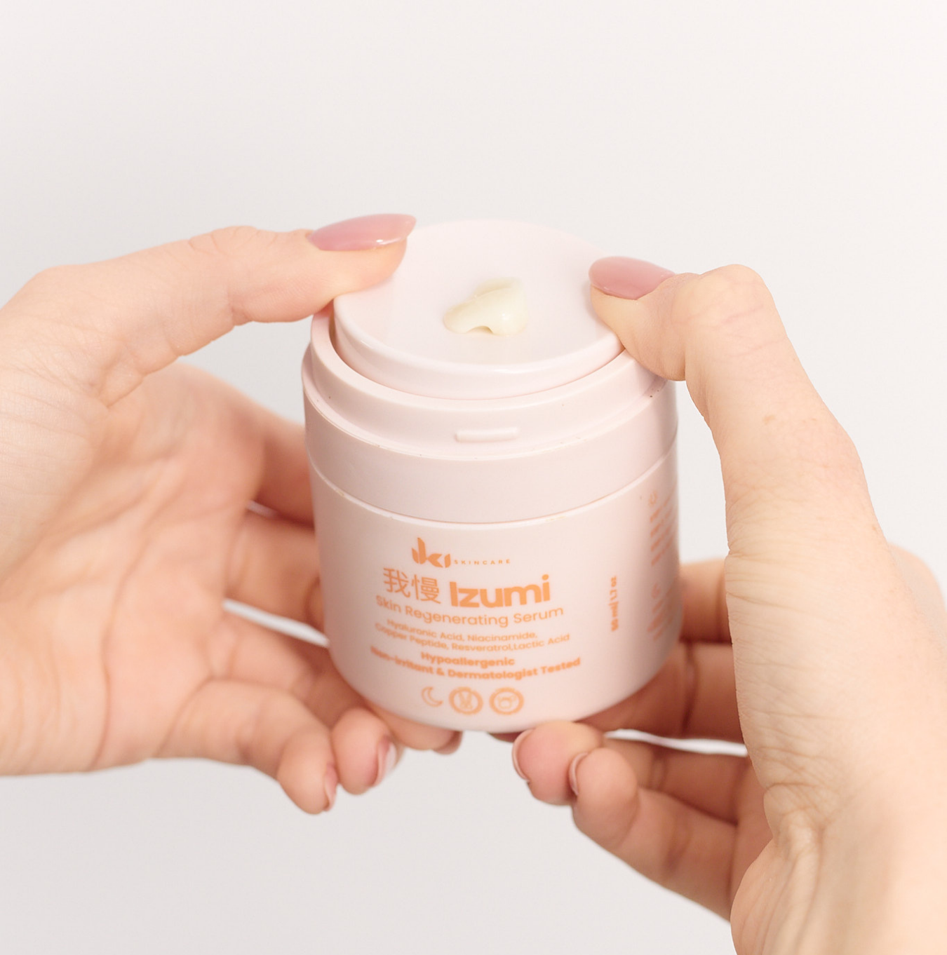 Hands holding a jar of Izumi Skin Regenerating Serum.