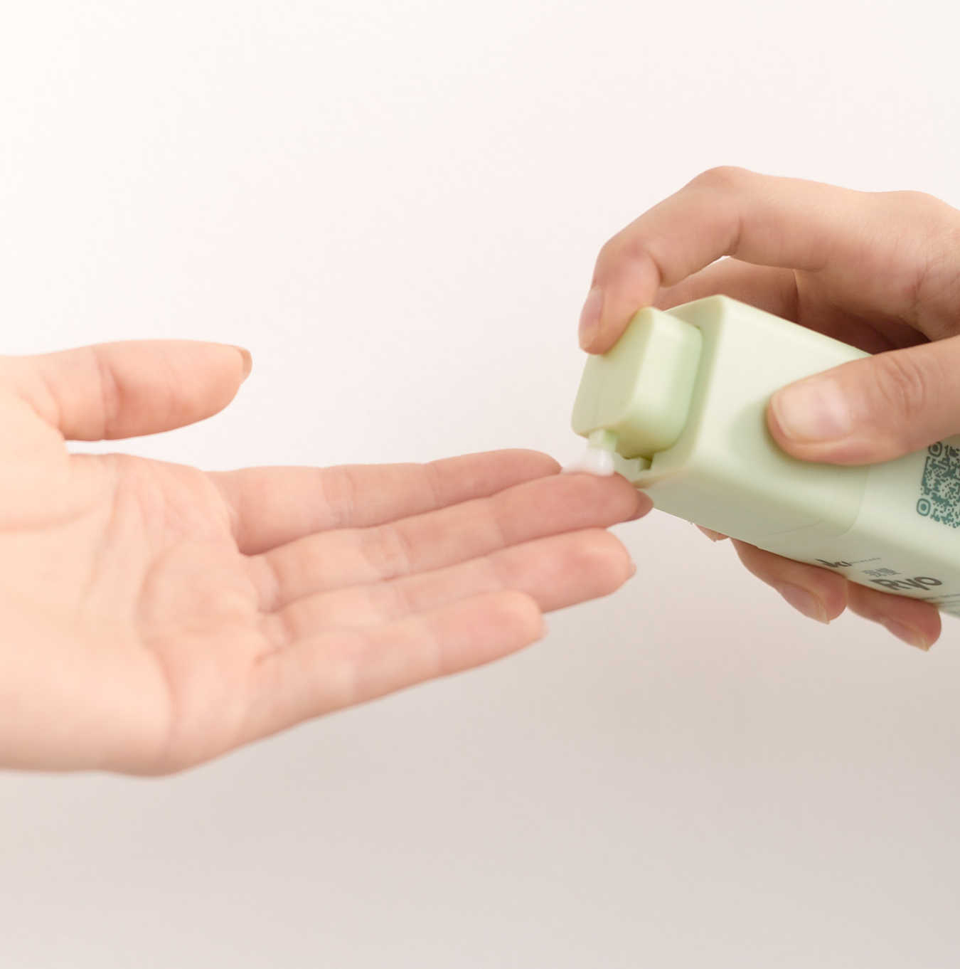 Hands dispensing lotion from a green bottle.