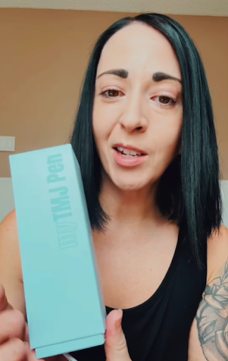 Person holding a blue box labeled 'TMJ Pen.'