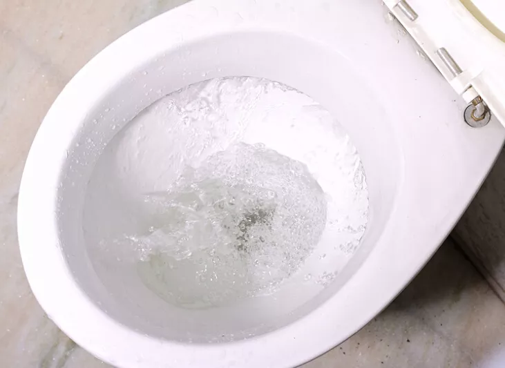 A close-up view of a white toilet bowl as it is being flushed, with the water swirling.
