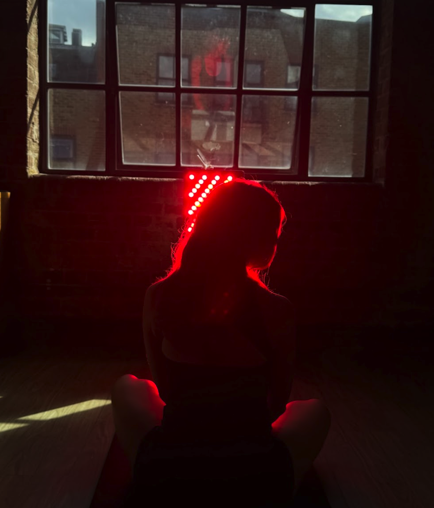 A person wearing a red LED headband sits silhouetted on the floor in front of a window.