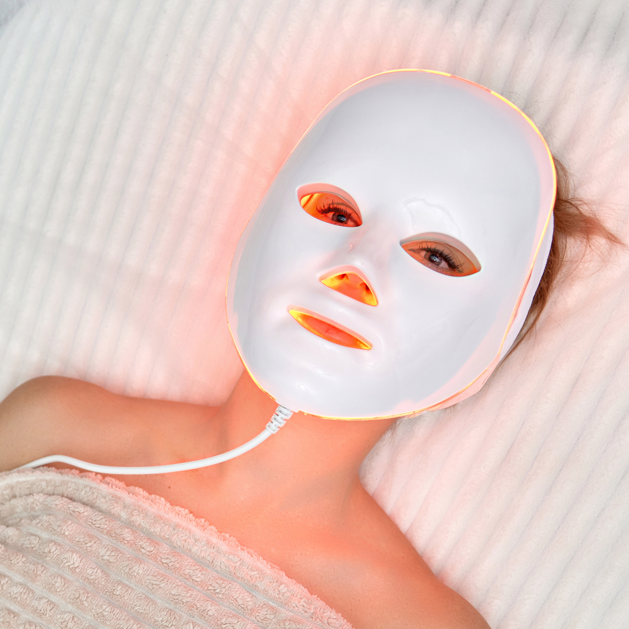 Person wearing a glowing white LED facial mask lying down.