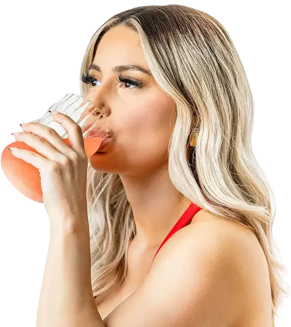 A woman with long blonde hair drinking a pink beverage from a clear glass.