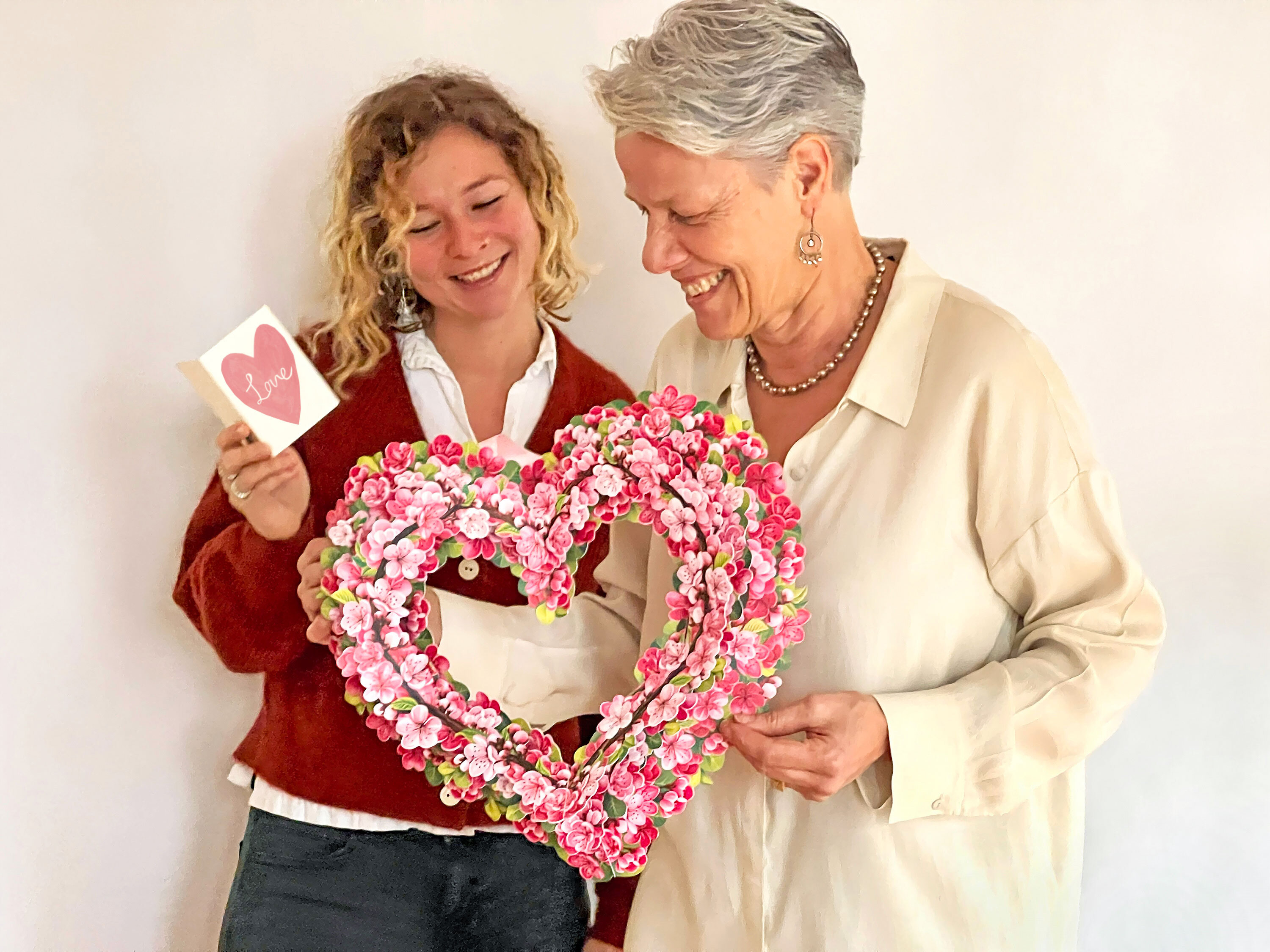 Two people smiling, holding a floral heart and a card with 'love' on it.
