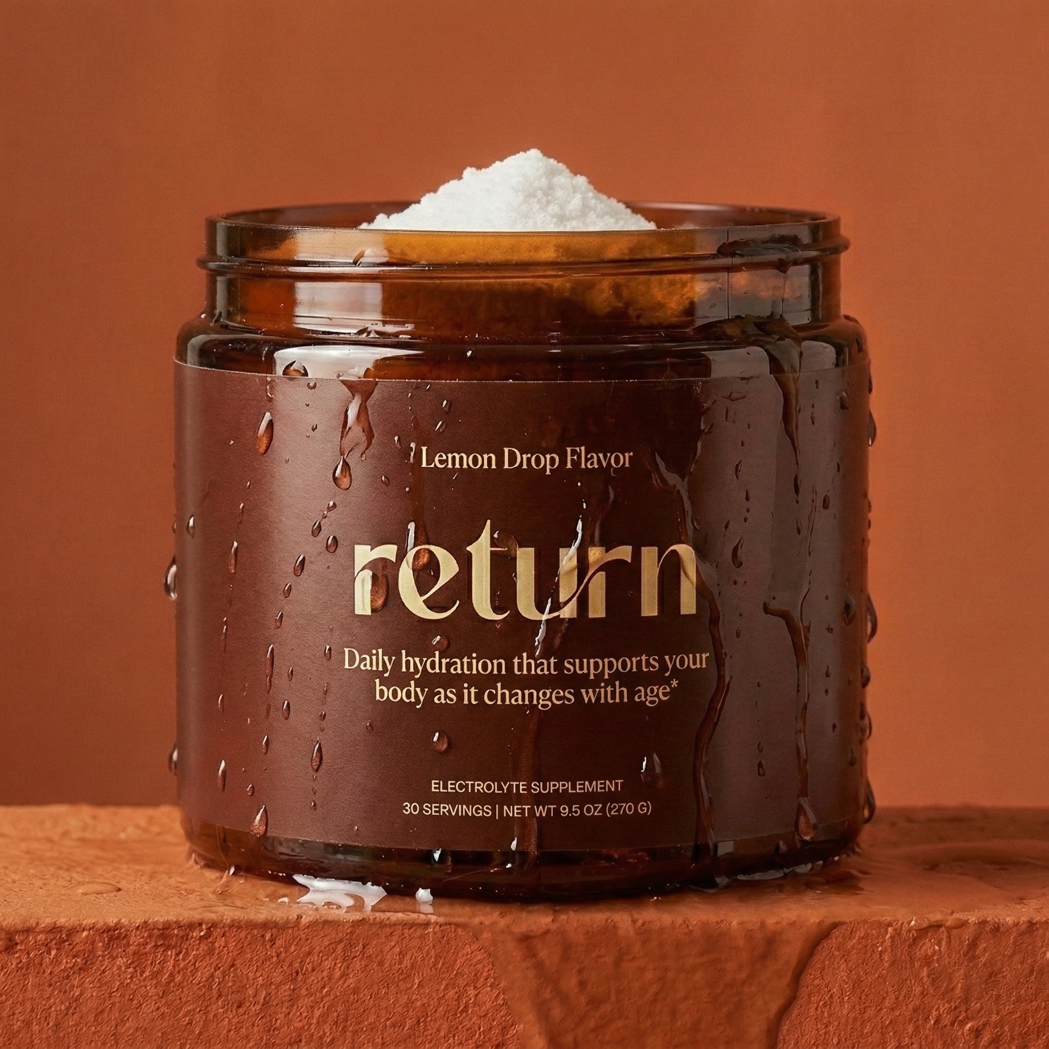 A wet, amber-colored jar of 'Return Lemon Drop' sits on a terracotta surface against a matching background.