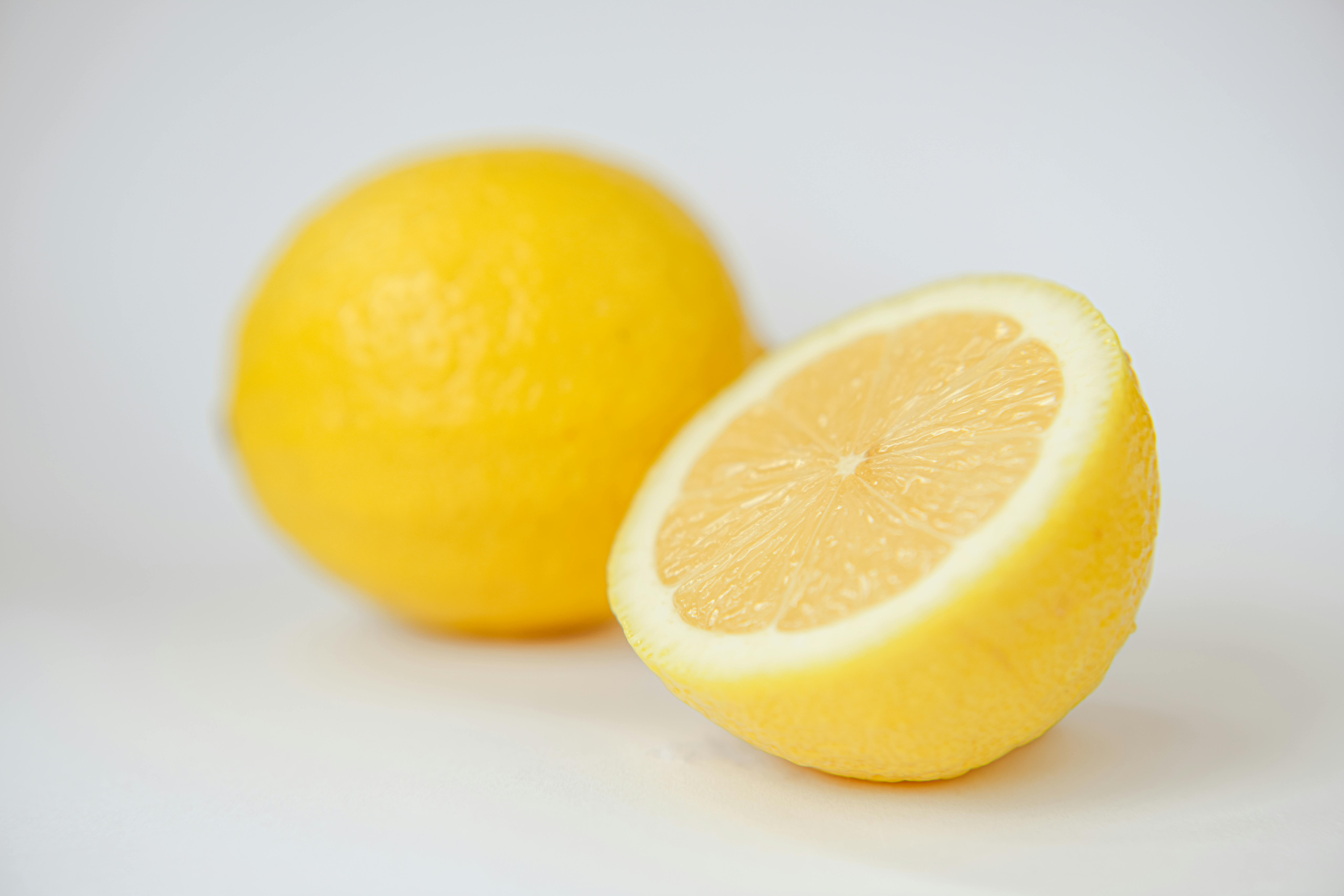 A whole lemon and a half lemon sit on a white surface with a shallow depth of field.