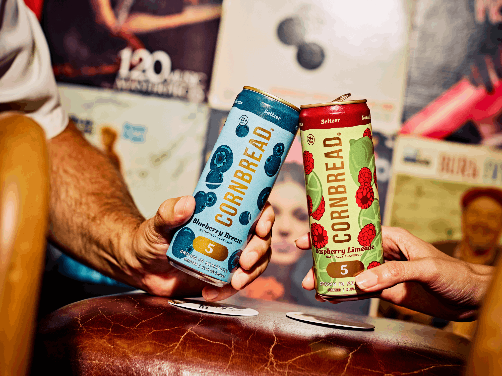 Two people clinking cans labeled 'Cornbread' with flavored seltzer drinks.