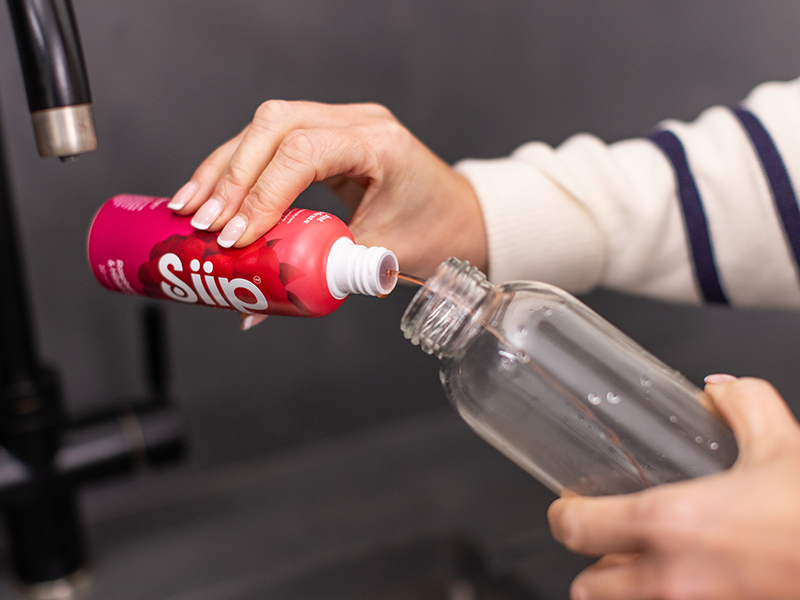 Person pouring liquid from a pink bottle into a clear bottle.