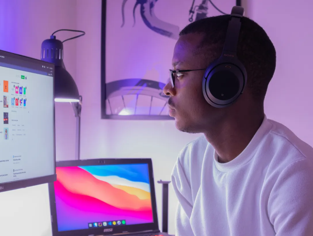 Person wearing headphones, sitting at a desk with computer monitors.