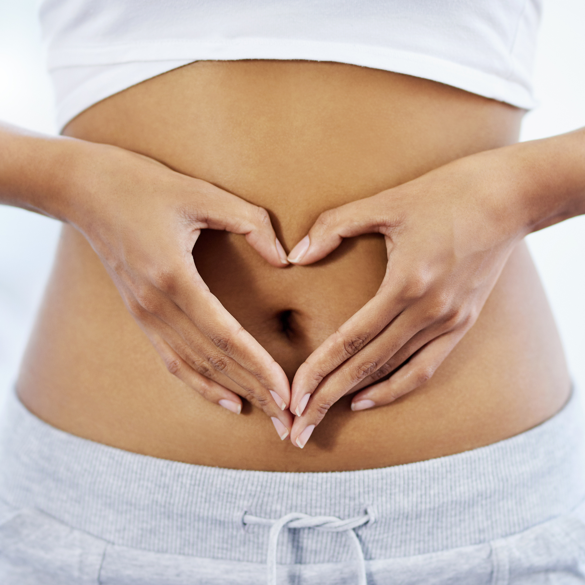 Hands forming a heart shape on a bare stomach.