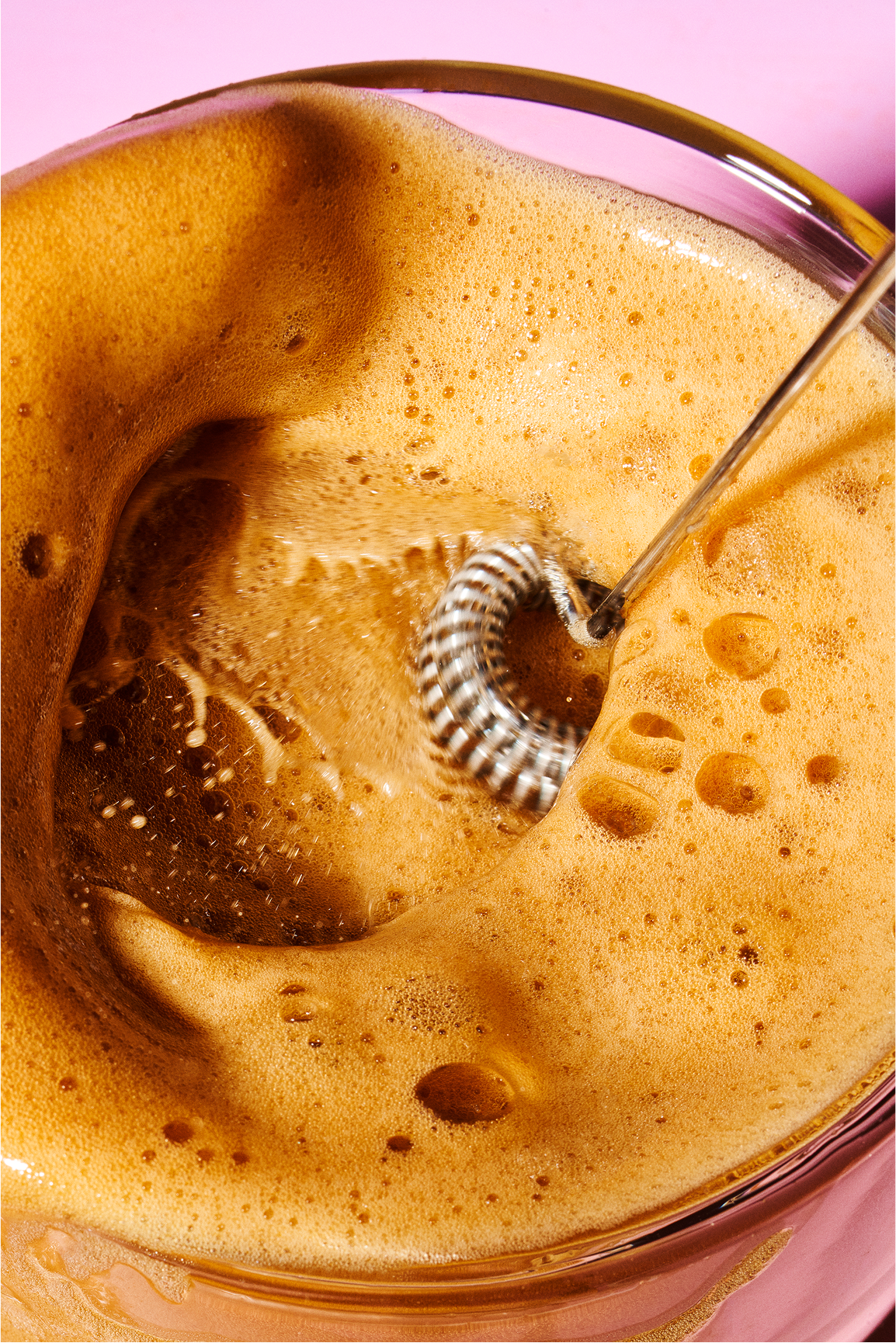 Close-up of frothy coffee being whisked in a glass bowl.