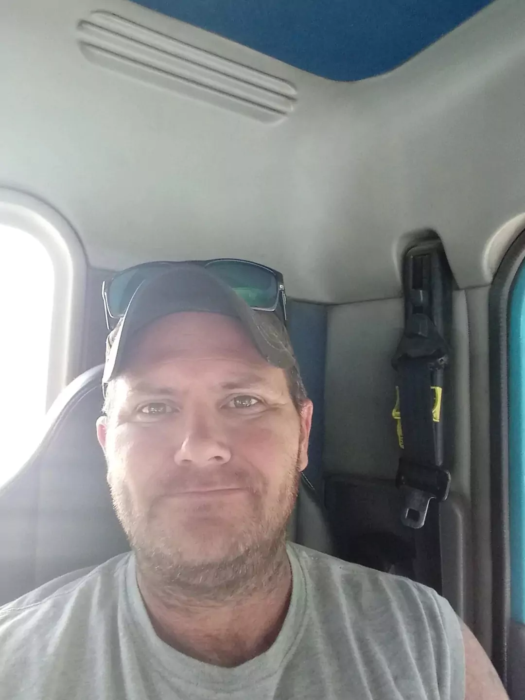 Man wearing a cap and sunglasses inside a vehicle.