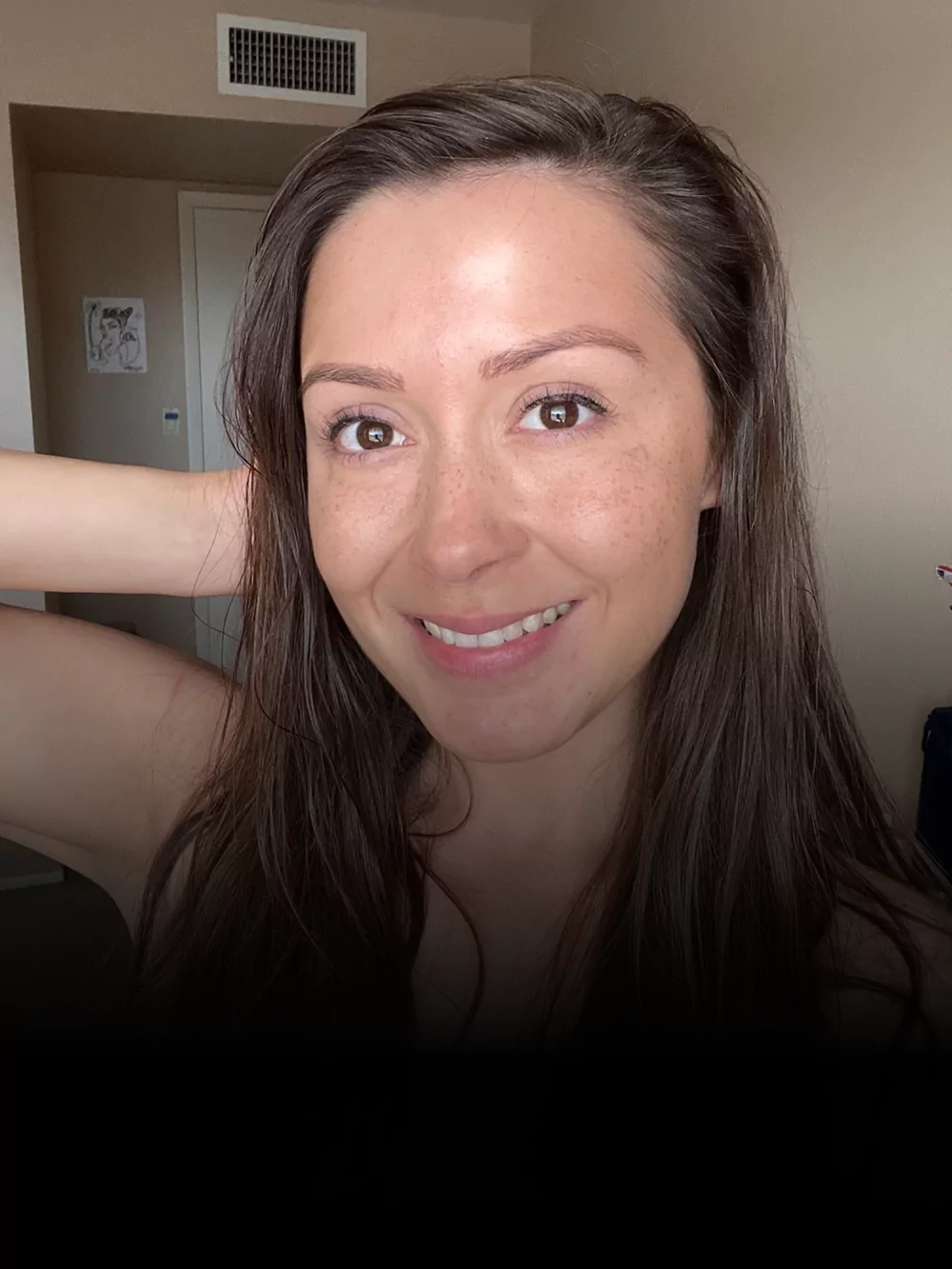 A person smiling indoors with long brown hair and a light background.