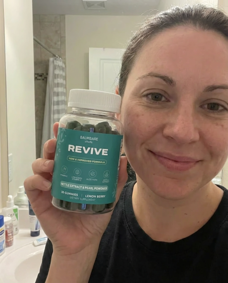 A woman with brown hair smiles while holding a clear bottle of Balmbare Revive gummies in a bathroom.