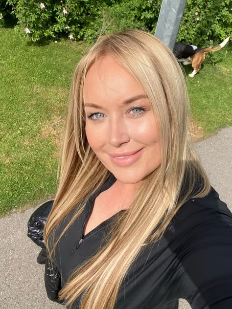 Person with long blonde hair smiling outdoors on a sunny day.