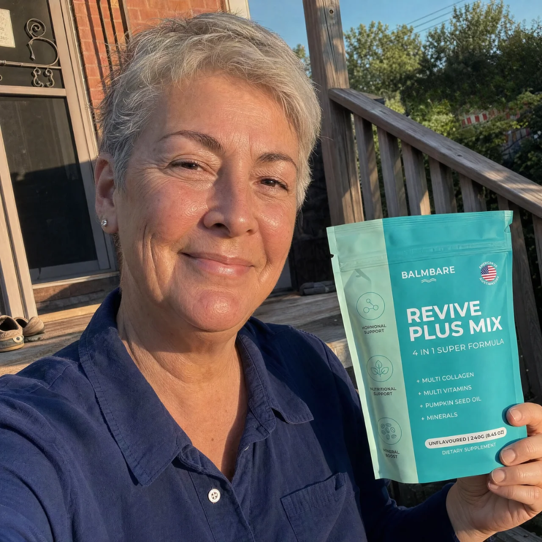 A smiling woman with short gray hair holds up a pouch of Balmbare Revive Plus Mix outdoors.