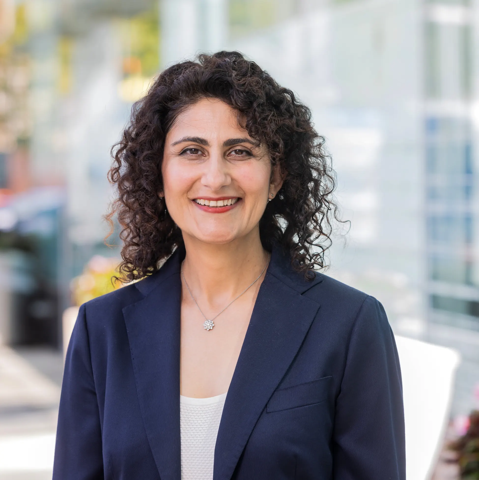 Smiling person with curly hair in a navy blazer outdoors.