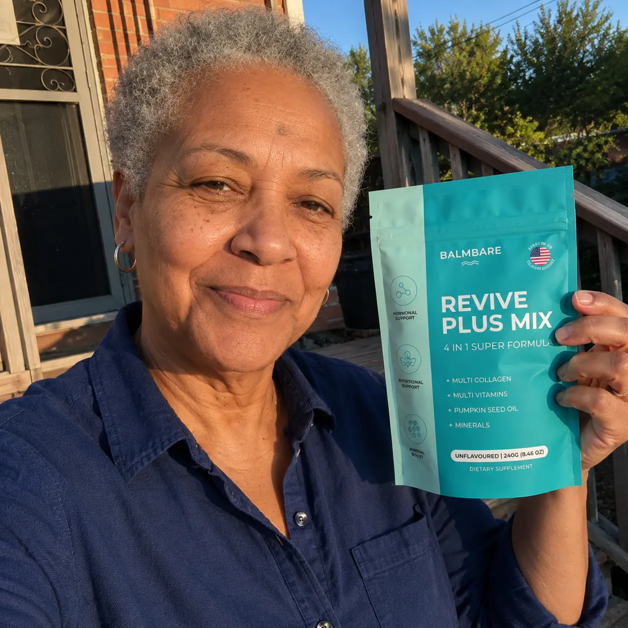 A woman with short gray hair smiles while holding a teal pouch of Revive Plus Mix dietary supplement.