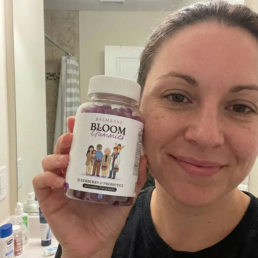 A smiling woman in a bathroom holds up a bottle of Balmbare Bloom Gummies.