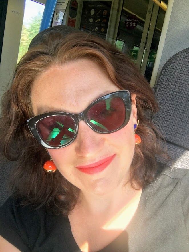 Person with sunglasses and earrings smiling inside a train.