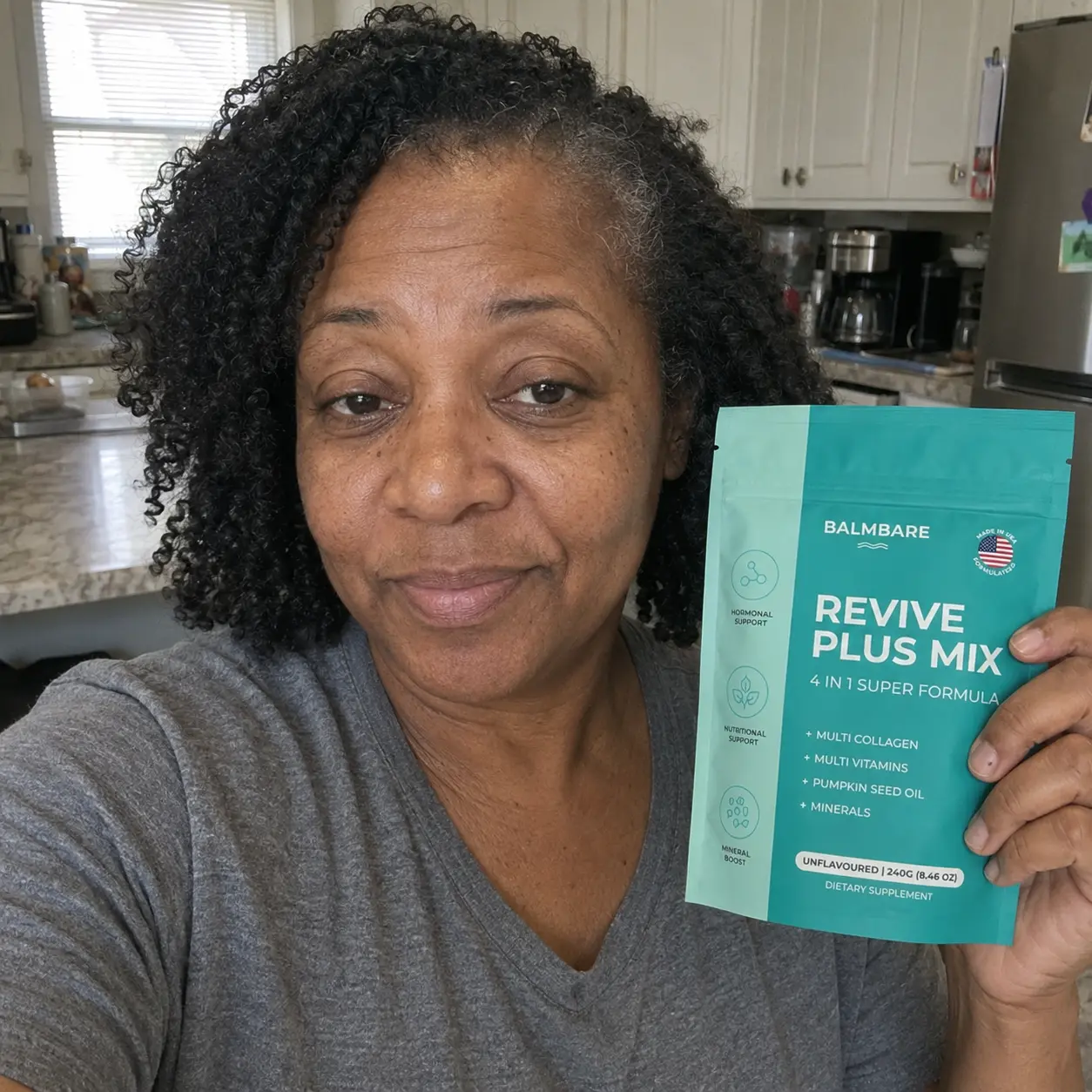 A smiling woman with short gray hair holds up a pouch of Balmbare Revive Plus Mix outdoors.