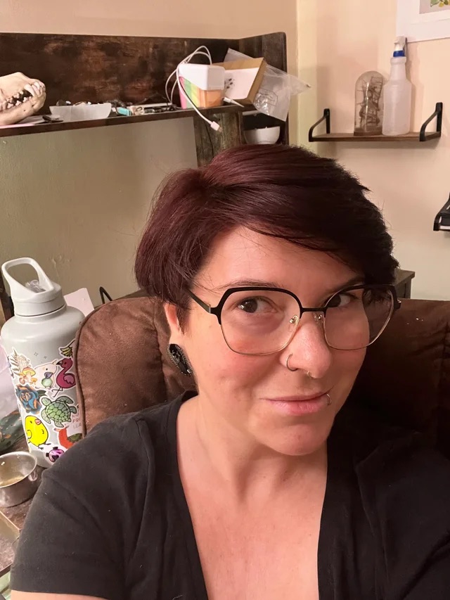Person with glasses and short hair, sitting indoors with a decorated water bottle nearby.