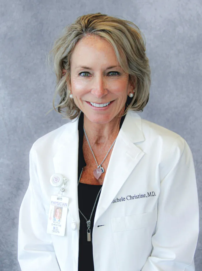 Person in a white coat with a name tag, smiling at the camera.