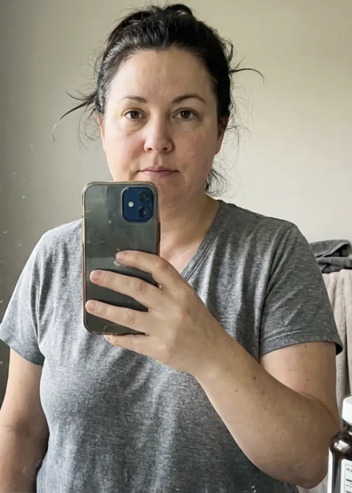 A woman in a grey t-shirt takes a selfie in a mirror with her smartphone.