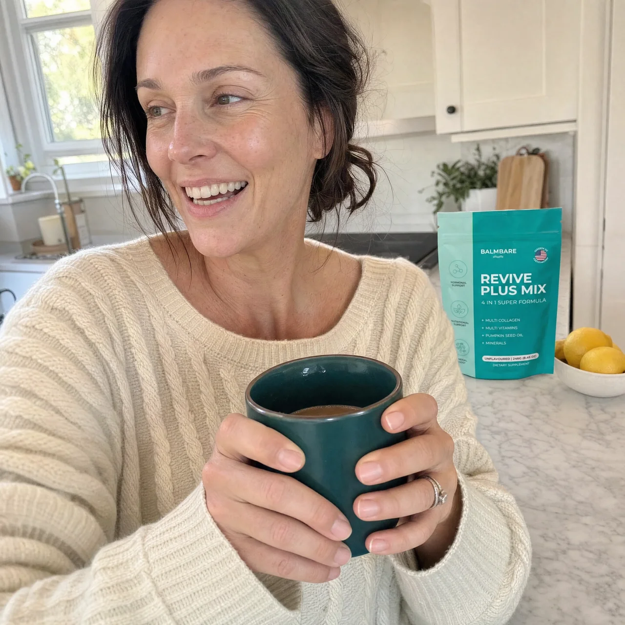 A smiling woman in a sweater holds a mug in a kitchen with a supplement packet on the counter.