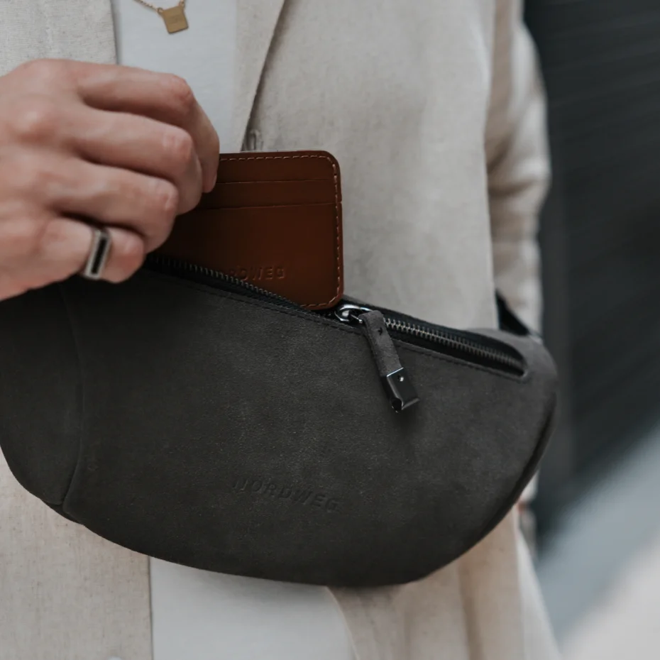 Mão guarda uma carteira de couro no bolso com zíper da Sling Bag Pulse Limited Edition Nordweg na cor Dark Steel