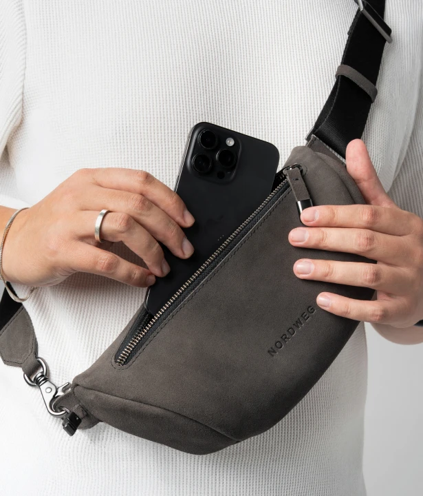 Mão guarda um smartphone no compartimento com zíper da Sling Bag Pulse Limited Edition Nordweg usada transversalmente