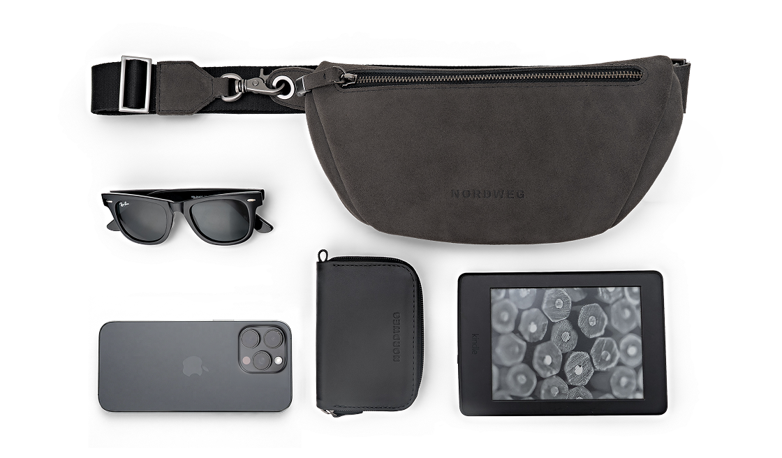 Flat lay da Sling Bag Pulse Limited Edition Nordweg na cor Dark Steel ao lado de óculos, smartphone, carteira de couro e leitor digital