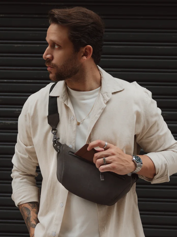 Homem de camisa clara guarda uma carteira de couro na Sling Bag Pulse Limited Edition Nordweg na cor Dark Steel usada transversalmente