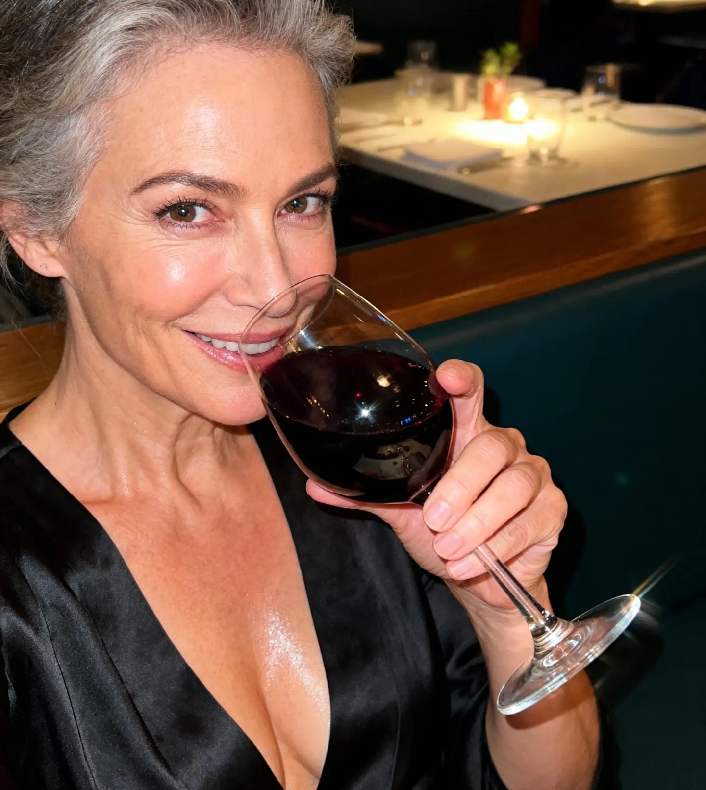 Person holding a glass of red wine, smiling at the camera in a restaurant setting.