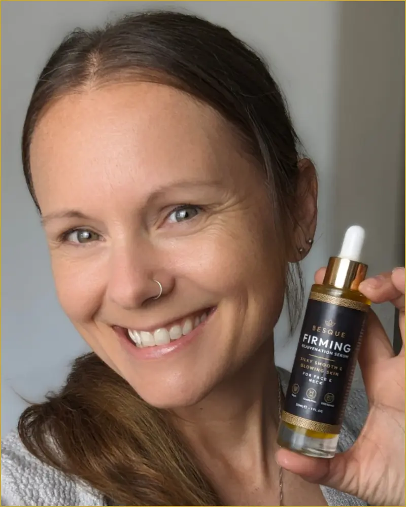 Person smiling and holding a bottle labeled 'firming rejuvenation serum.'