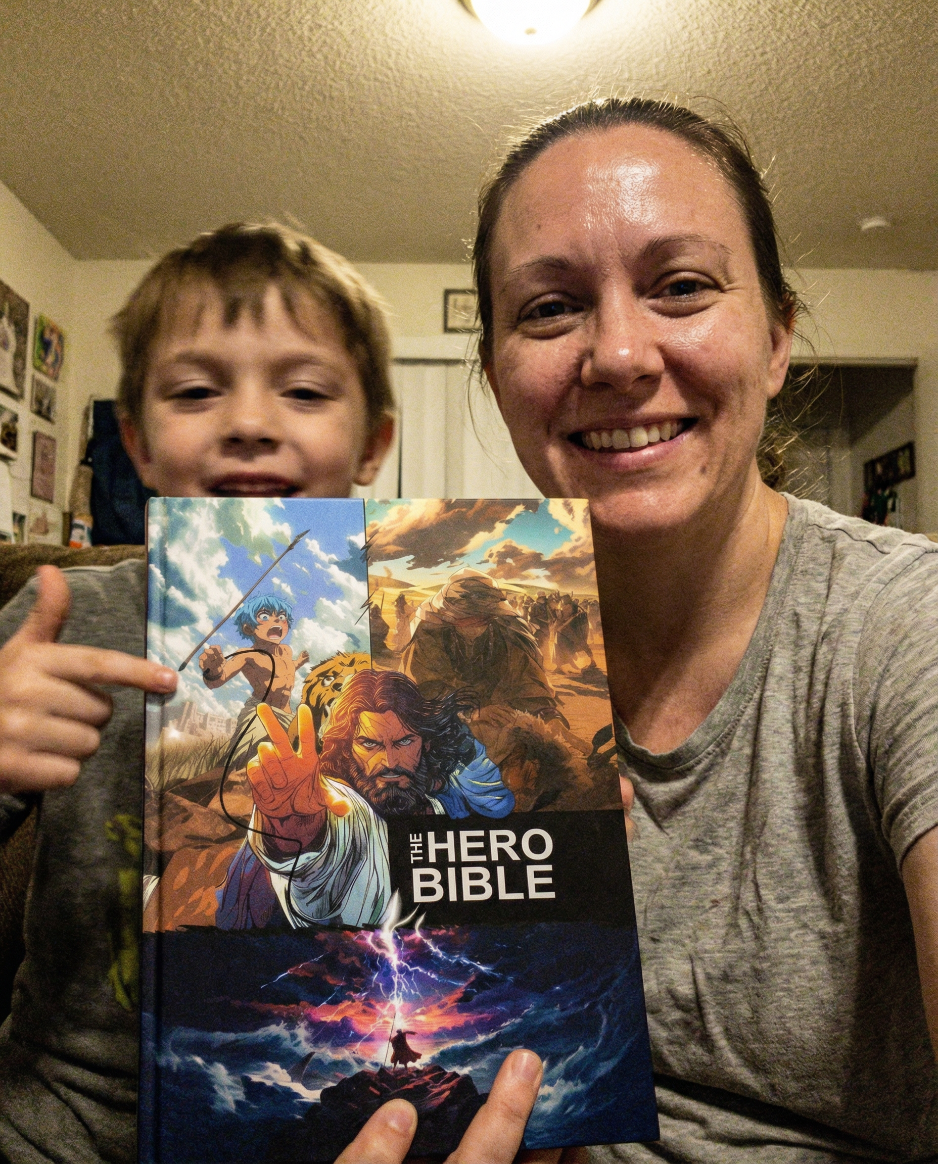 A woman and a young boy smile while holding a book titled 'The Hero Bible'.