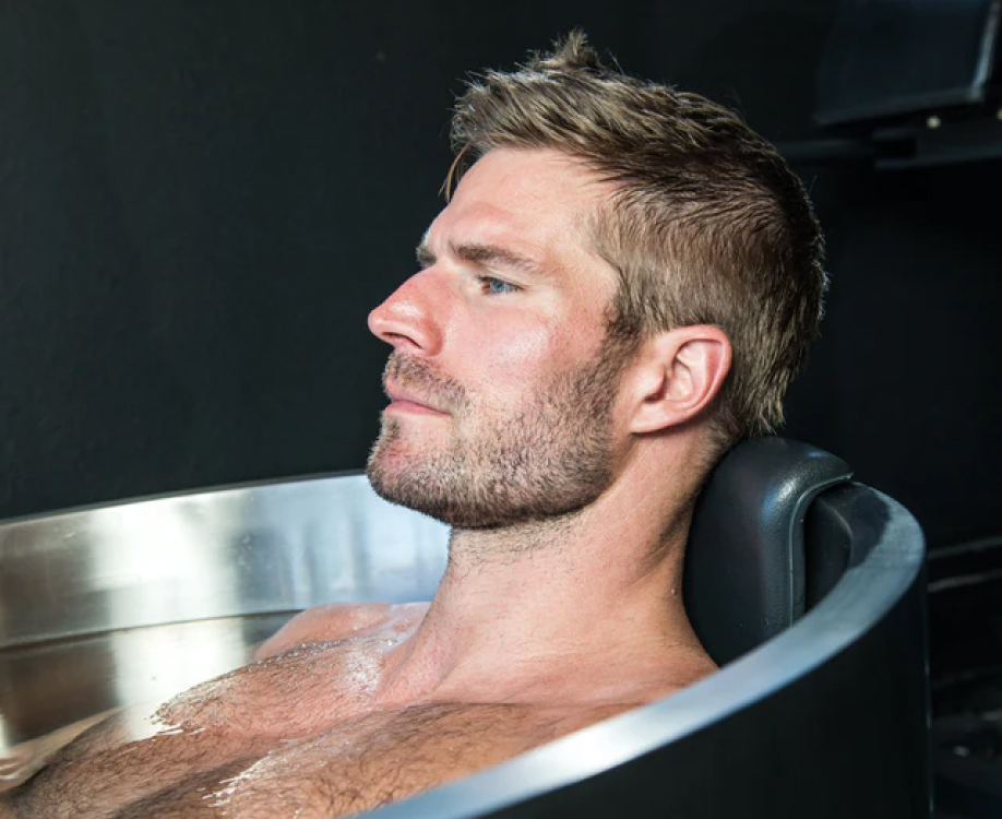Man relaxing in a metal bathtub, head resting on a black cushion.